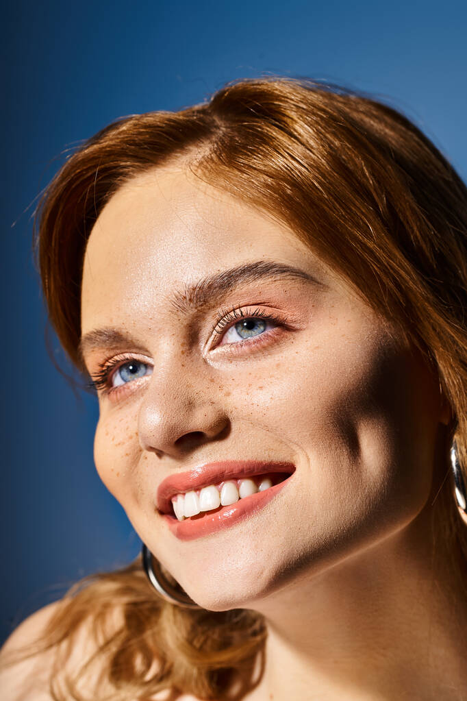 Closeup beauty shot of smiling woman with blue eyes, peach makeup and freckles on blue background - Photo, Image