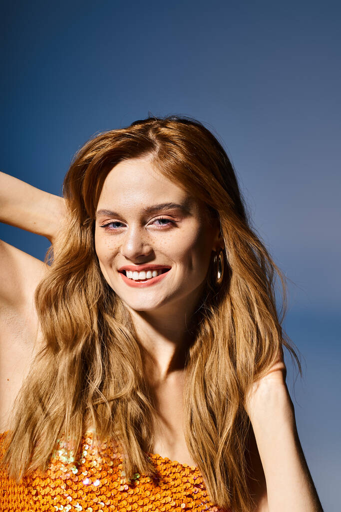Piękne ujęcie radosnej młodej kobiety uśmiechniętej, dotykającej włosów na ciemnoniebieskim tle - Zdjęcie, obraz