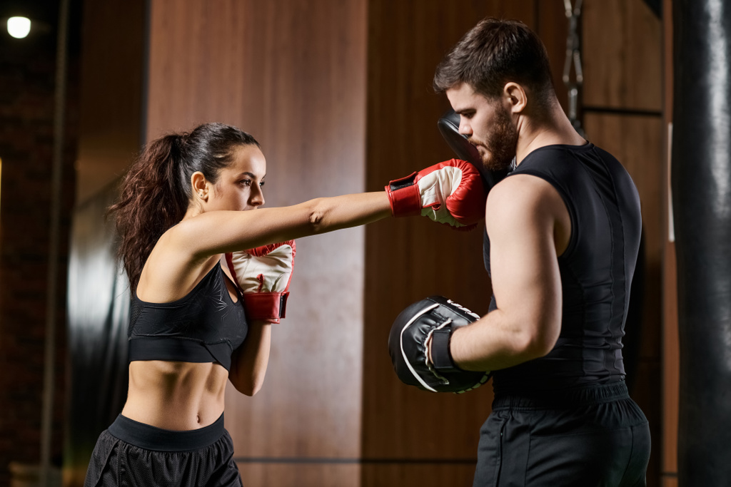 Een mannelijke trainer begeleidt een brunette sporter in actieve kleding als ze zich bezighouden met bokstraining in een fitnessruimte. - Foto, afbeelding