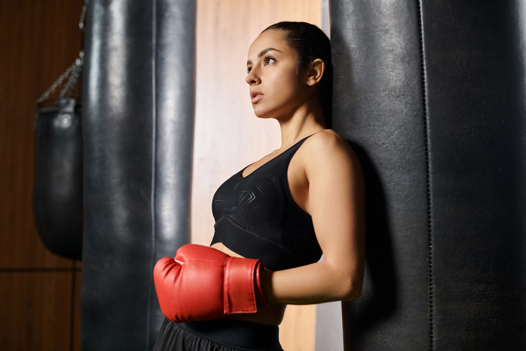 Brunetka sportowiec pokazuje siłę i siłę boksu w siłowni, ubrana w czarny top i żywe czerwone rękawice bokserskie. - Zdjęcie, obraz