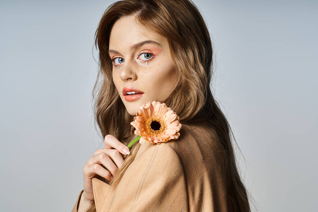 Portrait of attractive woman looking at camera and holding daisy, wearing peach makeup, face jewels - Photo, Image