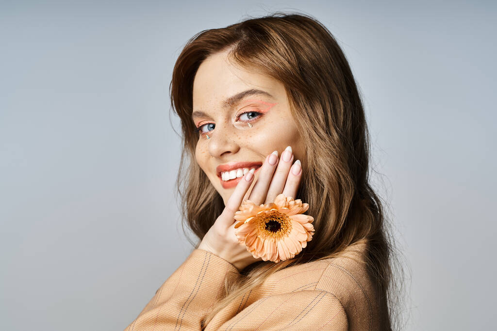 Kauneus muotokuva kaunis nainen kasvojen jalokivet meikki ja kukka koskettaa kasvot harmaalla pohjalla - Valokuva, kuva