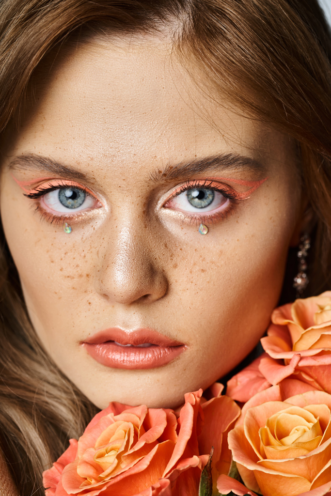 Primer plano de belleza de la mujer con maquillaje de melocotón, joyas de la cara y pecas, la celebración de rosas cerca de la mejilla - Foto, imagen