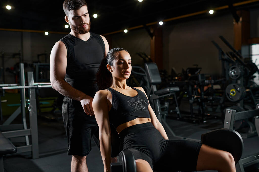 Een mannelijke trainer staat naast een brunette sportvrouw in een sportschool, assisteren met een workout routine. - Foto, afbeelding