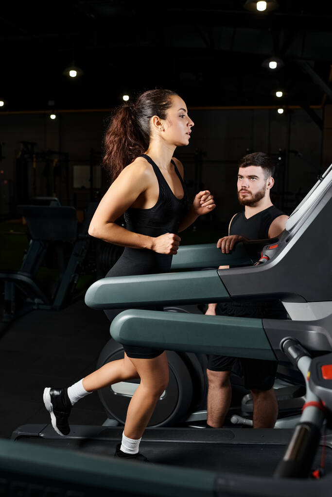 Muž trenér motivuje brunetka sportovkyně, jak běží spolu na běžeckém pásu v posilovně nastavení. - Fotografie, Obrázek