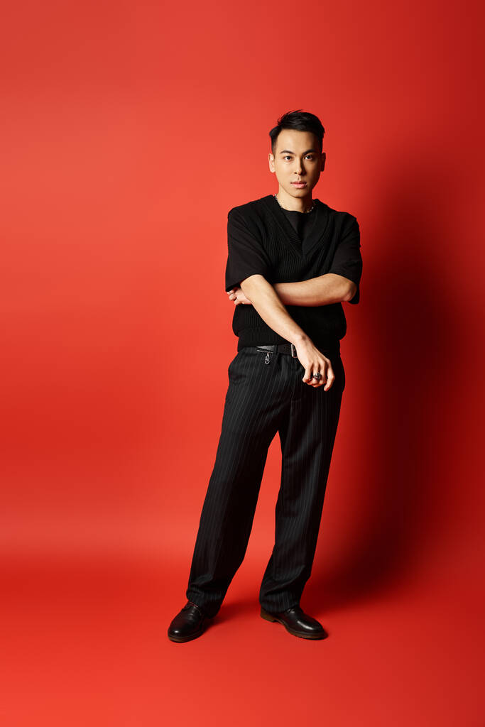 Ένας κομψός και όμορφος Ασιάτης στέκεται με αυτοπεποίθηση μπροστά σε ένα τολμηρό κόκκινο φόντο σε ένα σκηνικό στούντιο. - Φωτογραφία, εικόνα