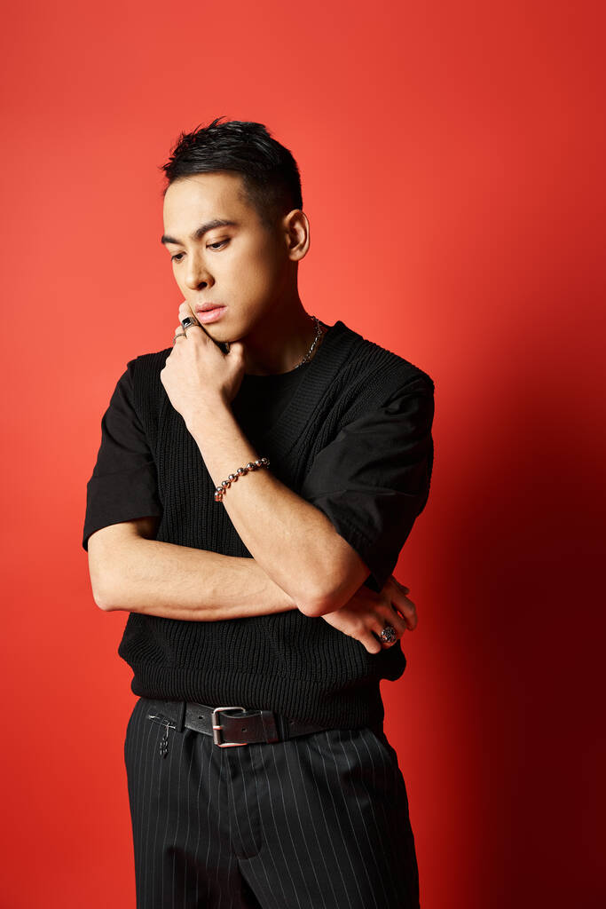 Knappe Aziatische man in zwart shirt staat zelfverzekerd tegen levendige rode achtergrond in studio setting. - Foto, afbeelding