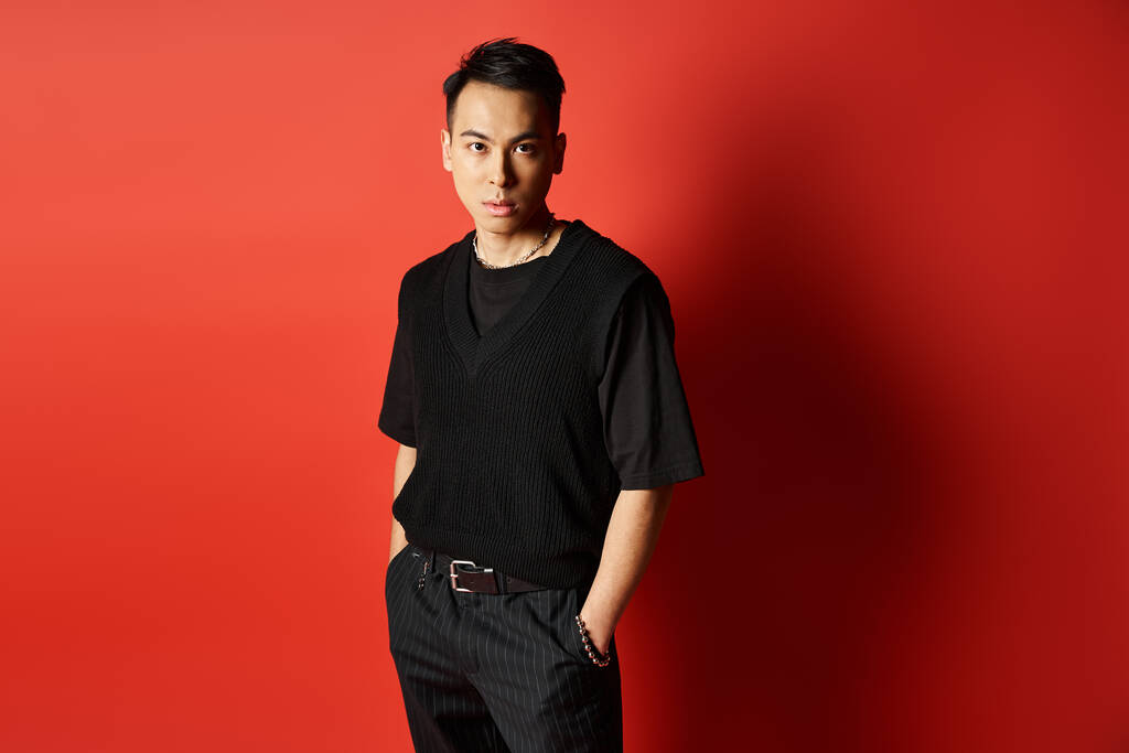 Ein stilvoller und gut aussehender asiatischer Mann steht selbstbewusst vor einer auffallend roten Wand in einem Studio-Setting. - Foto, Bild