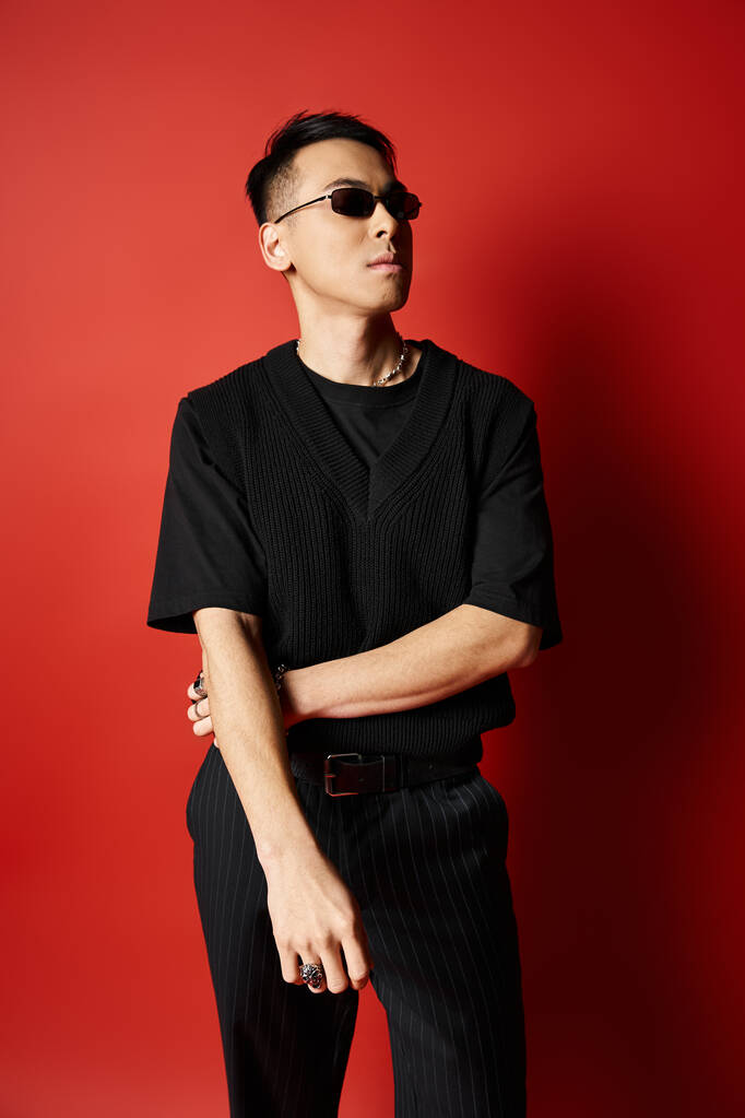 Egy elegáns és jóképű ázsiai férfi fekete ingben és fekete nadrágban pózol egy merész vörös háttér előtt egy stúdióban.. - Fotó, kép