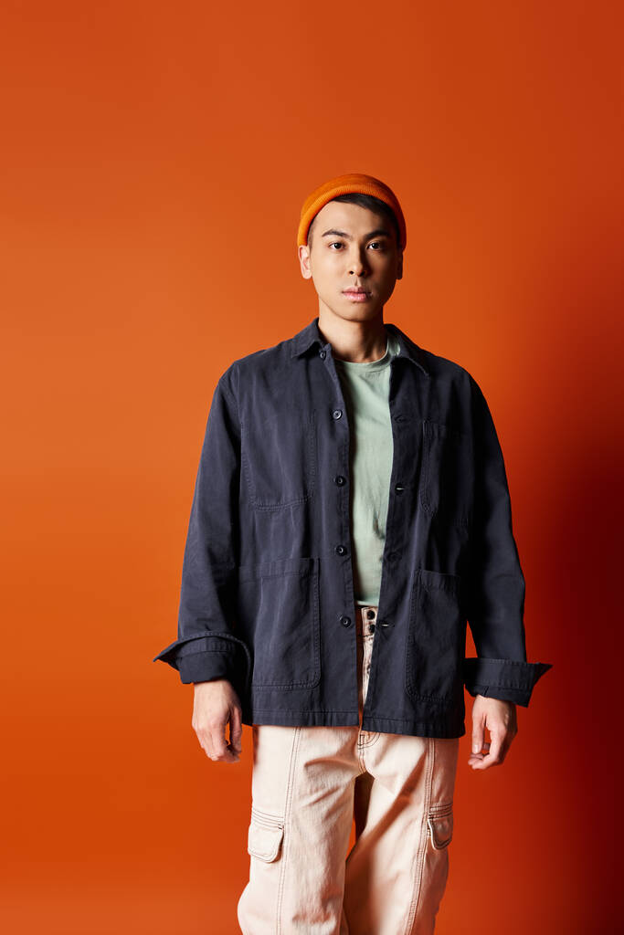 Красивий азіатський чоловік впевнено стоїть в стильному вбранні проти яскравої помаранчевої стіни в студійній обстановці. - Фото, зображення