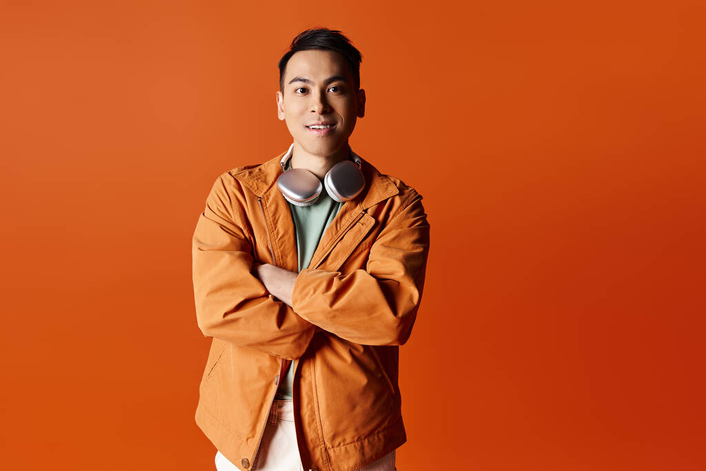 Jóképű ázsiai férfi elegáns öltözékben, karokkal keresztbe tett kézzel, élénk narancssárga háttér előtt, stúdió környezetben.. - Fotó, kép