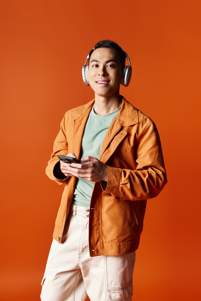 Un homme asiatique élégant portant des écouteurs, absorbé dans son téléphone portable. - Photo, image