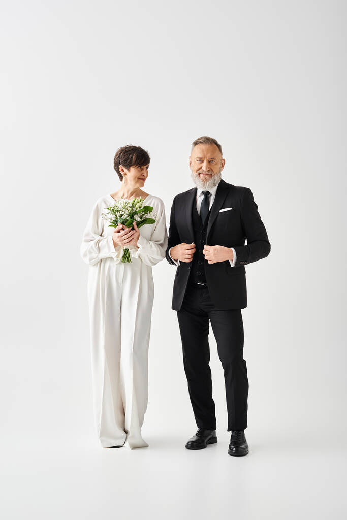Bruid en bruidegom van middelbare leeftijd in formele kledij staan samen in een studio en vieren hun speciale dag met liefde en elegantie. - Foto, afbeelding