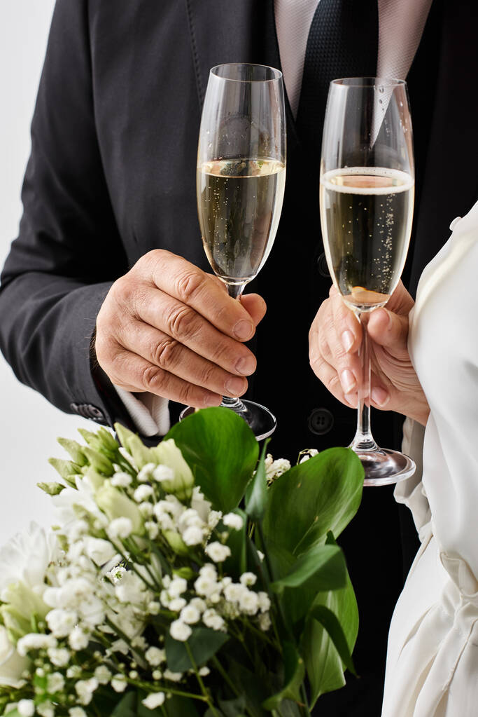 Novia y novio de mediana edad en traje de boda felizmente levantan flautas de champán en celebración. - Foto, Imagen