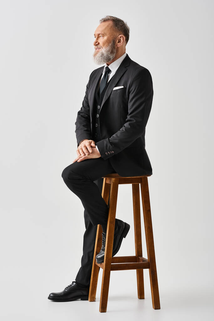 Middle-aged groom in an elegant suit sits on a stool in a studio setting, exuding timeless charm on his wedding day. - Photo, Image
