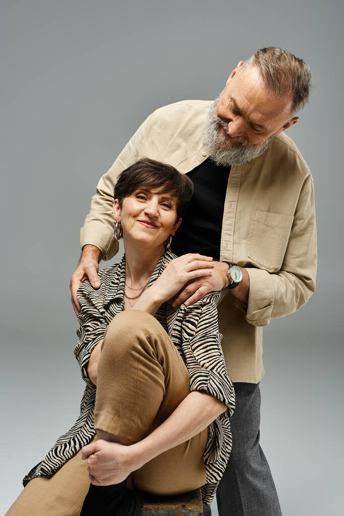 Un uomo di mezza età sostiene una donna sul retro di una sedia in un ambiente elegante studio, mettendo in mostra la fiducia e la partnership. - Foto, immagini