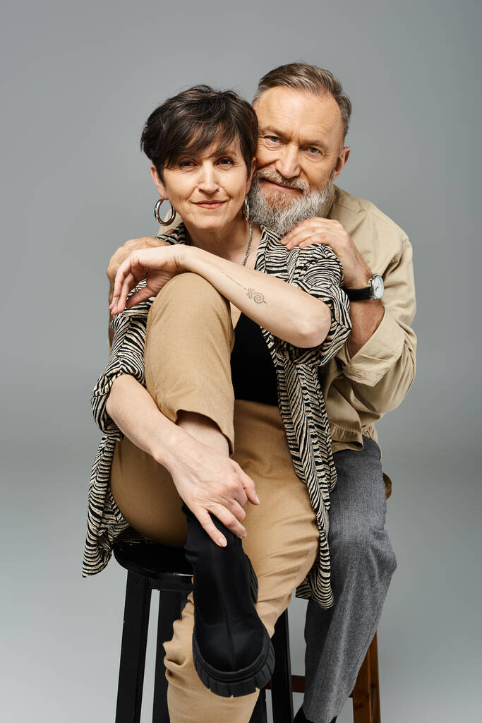 Un hombre y una mujer de mediana edad se posan en un taburete en un elegante entorno de estudio, comprometidos en la conversación y la conexión. - Foto, Imagen