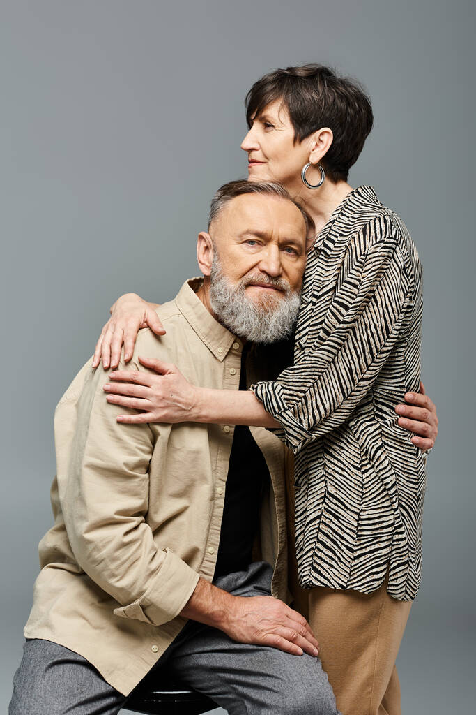 Egy középkorú férfi és nő, elegáns öltözékben, megosztják gyengéd ölelésüket egy stúdióban, bemutatva a szerelmet és a kapcsolatot.. - Fotó, kép
