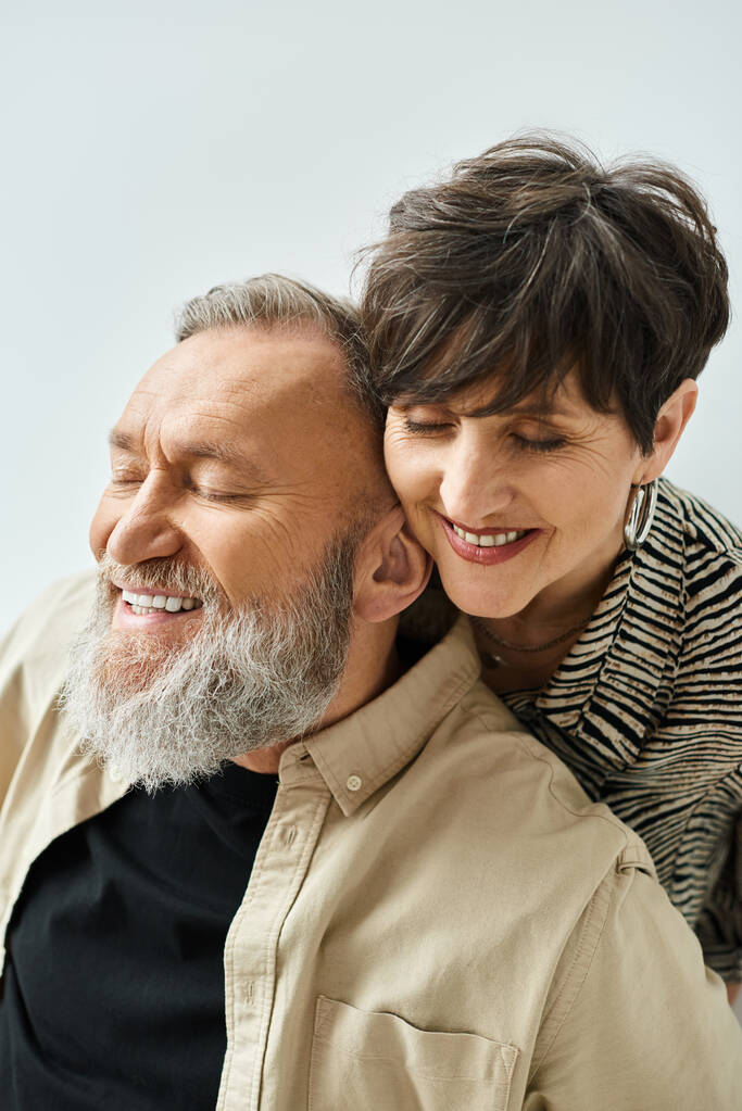 Un hombre y una mujer de mediana edad con un atuendo elegante, sonriendo calurosamente el uno al otro en un entorno de estudio. - Foto, imagen