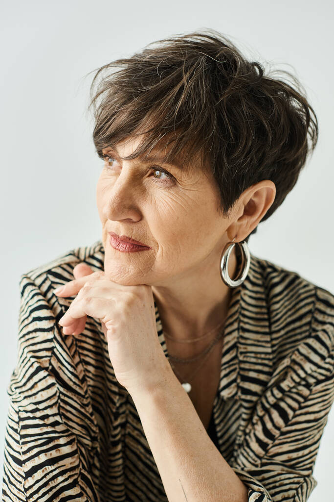 Женщина средних лет с короткими волосами в черно-белой рубашке излучает элегантность в студии. - Фото, изображение