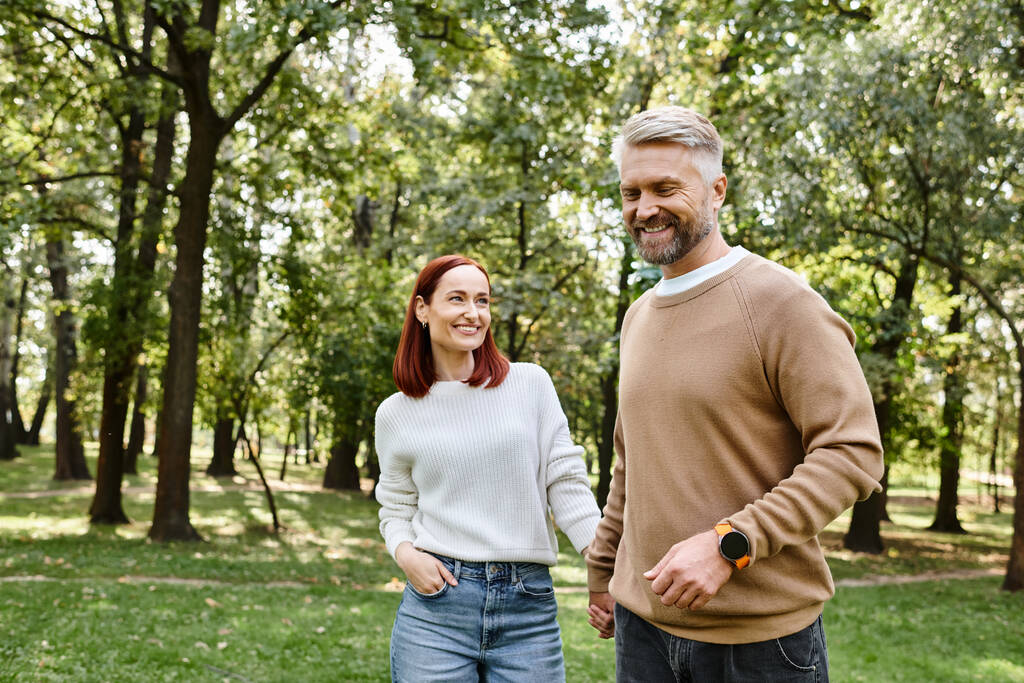 Una pareja adulta con un atuendo casual caminando tranquilamente por un parque. - Foto, Imagen
