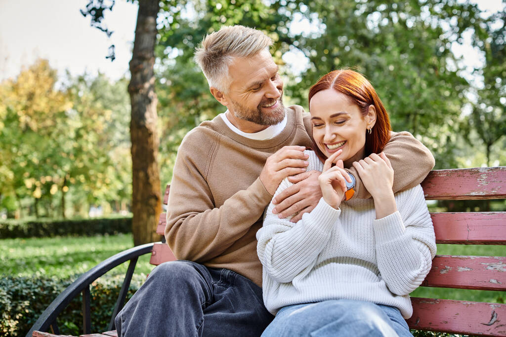 Couple aimant adulte en tenue décontractée se relaxant sur un banc de parc. - Photo, image