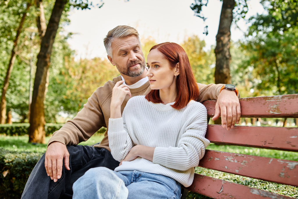 Un hombre y una mujer en atuendo casual se sientan tranquilamente juntos en un banco del parque. - Foto, imagen