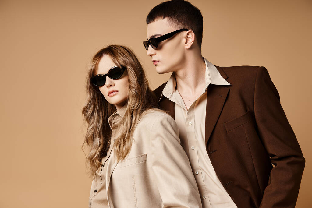 attraktives elegantes Paar in schicken saisonalen Anzügen mit stylischer Sonnenbrille posiert auf pastellfarbenem Hintergrund - Foto, Bild