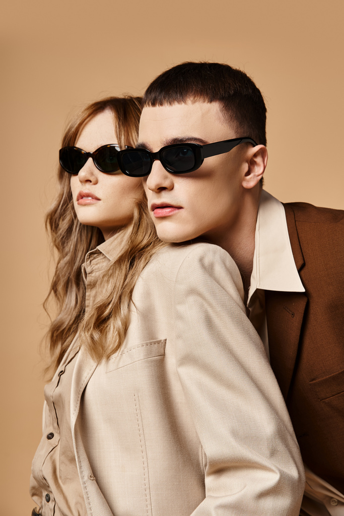aantrekkelijk elegant paar in chique seizoensgebonden pakken met stijlvolle zonnebril poseren op pastel achtergrond - Foto, afbeelding
