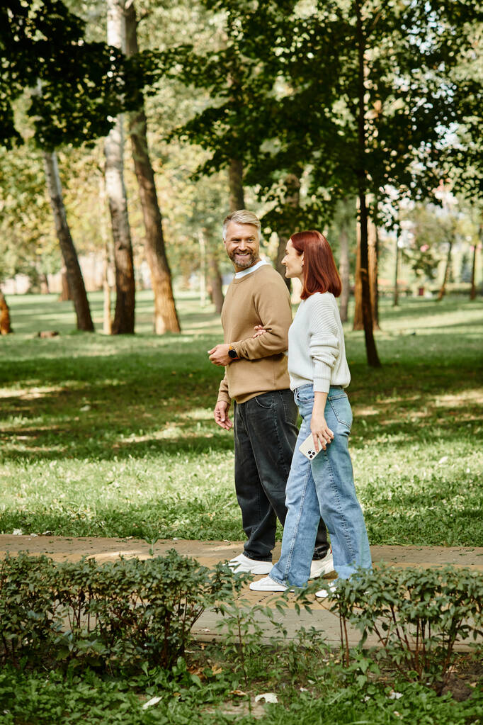Un homme et une femme, un couple amoureux, se promenant dans un parc en tenue décontractée. - Photo, image