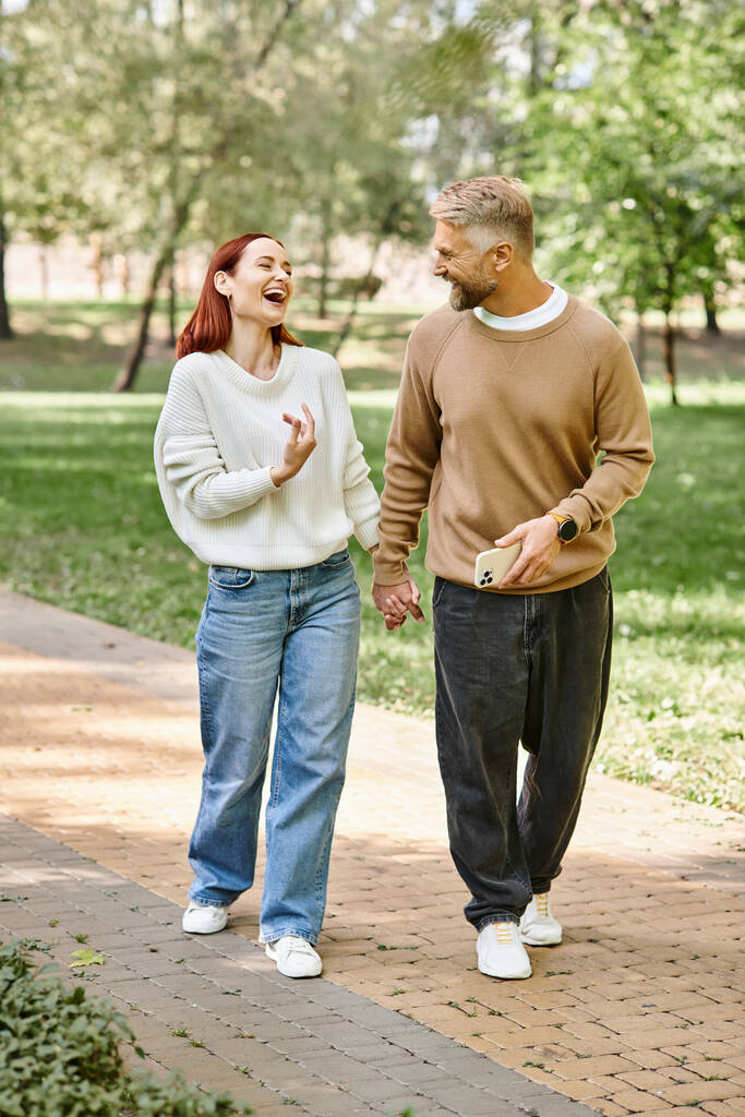 Un homme et une femme en tenue décontractée marchent ensemble sur un trottoir dans un parc. - Photo, image