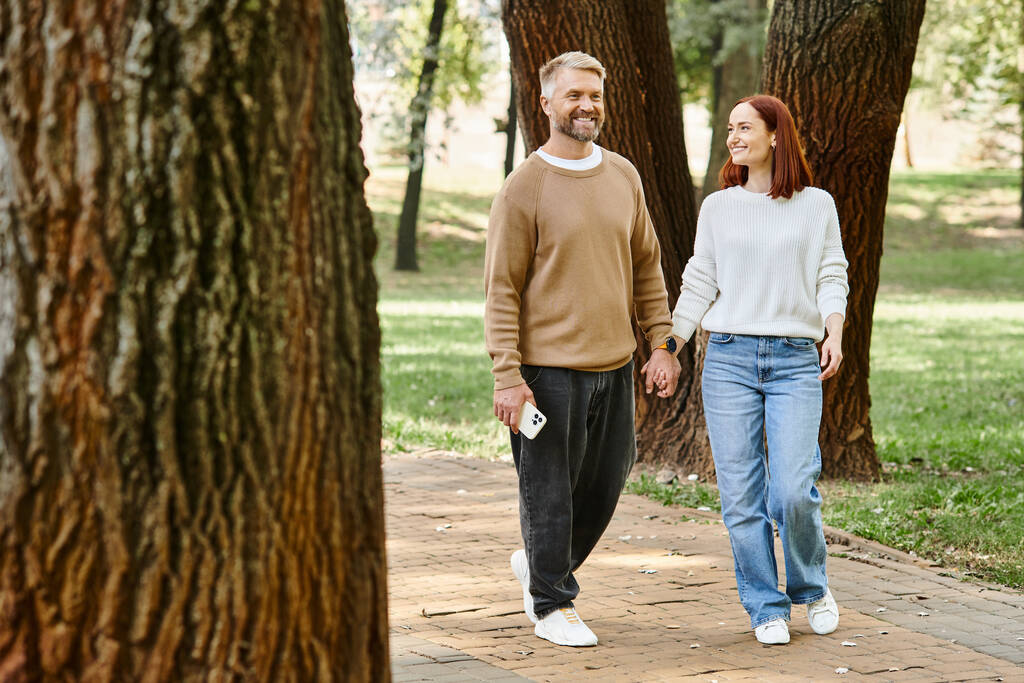 Egy férfi és egy nő alkalmi öltözékben sétálnak együtt egy békés parkban.. - Fotó, kép