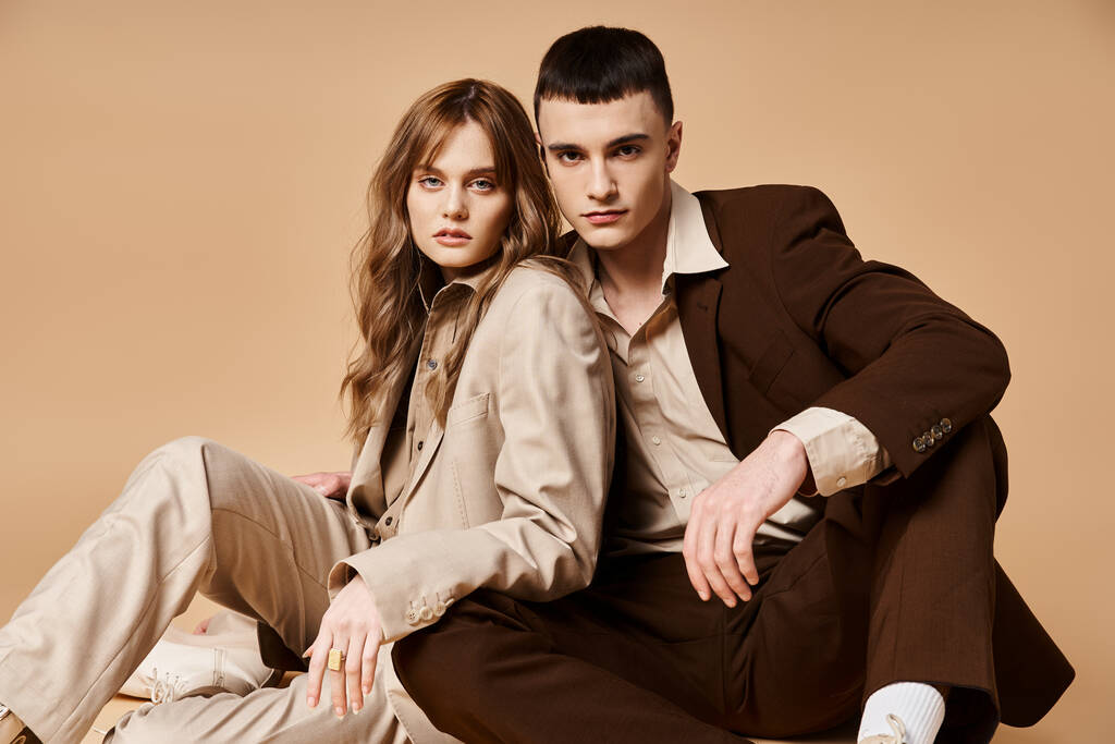 přitažlivý elegantní pár v elegantních oblecích sedí na podlaze a dívá se na kameru na pastelové pozadí - Fotografie, Obrázek