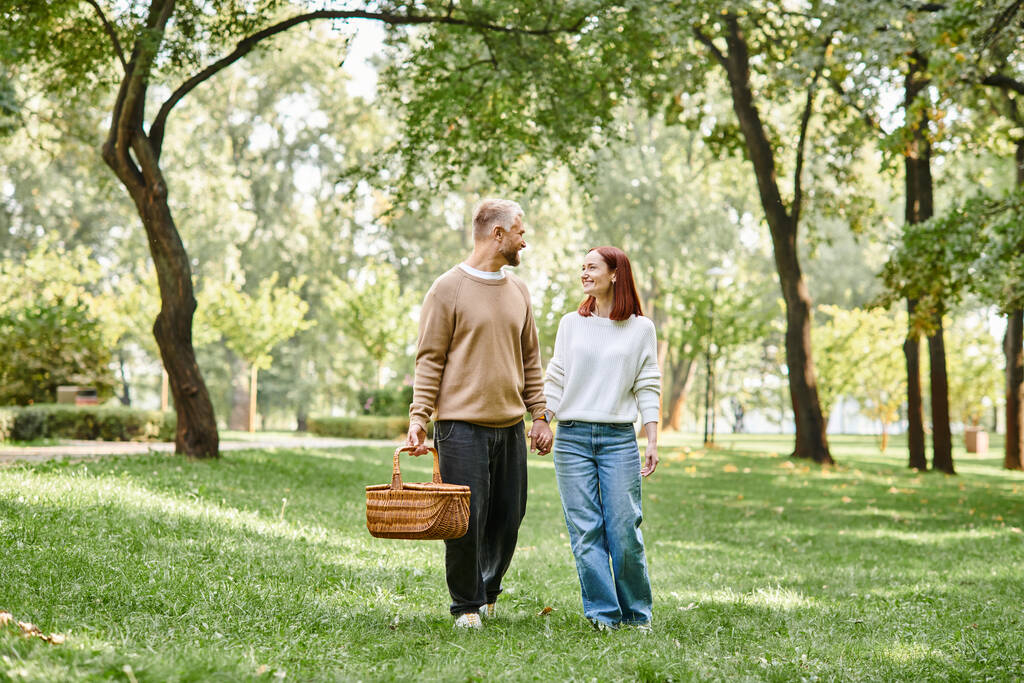 Un homme et une femme en tenue décontractée marchent main dans la main dans un parc paisible. - Photo, image
