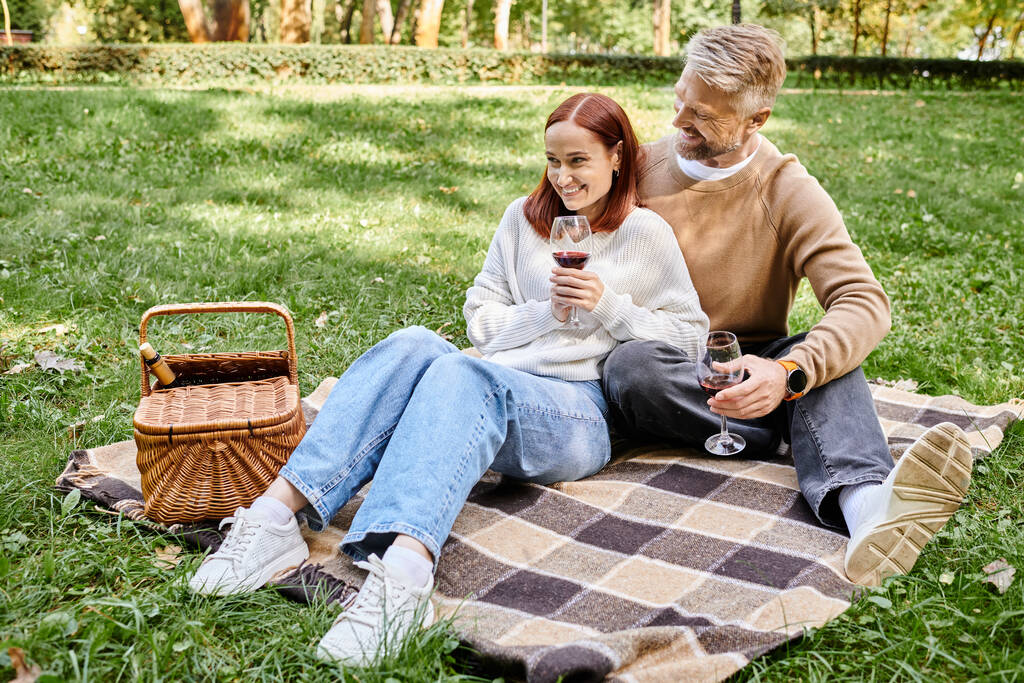Um homem e uma mulher de traje casual sentados em um cobertor na grama. - Foto, Imagem