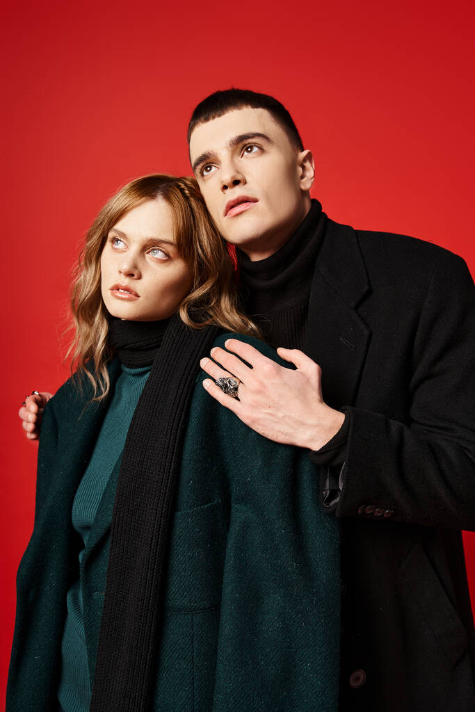 beautiful elegant couple in stylish coats posing together and looking away on vibrant backdrop - Photo, Image