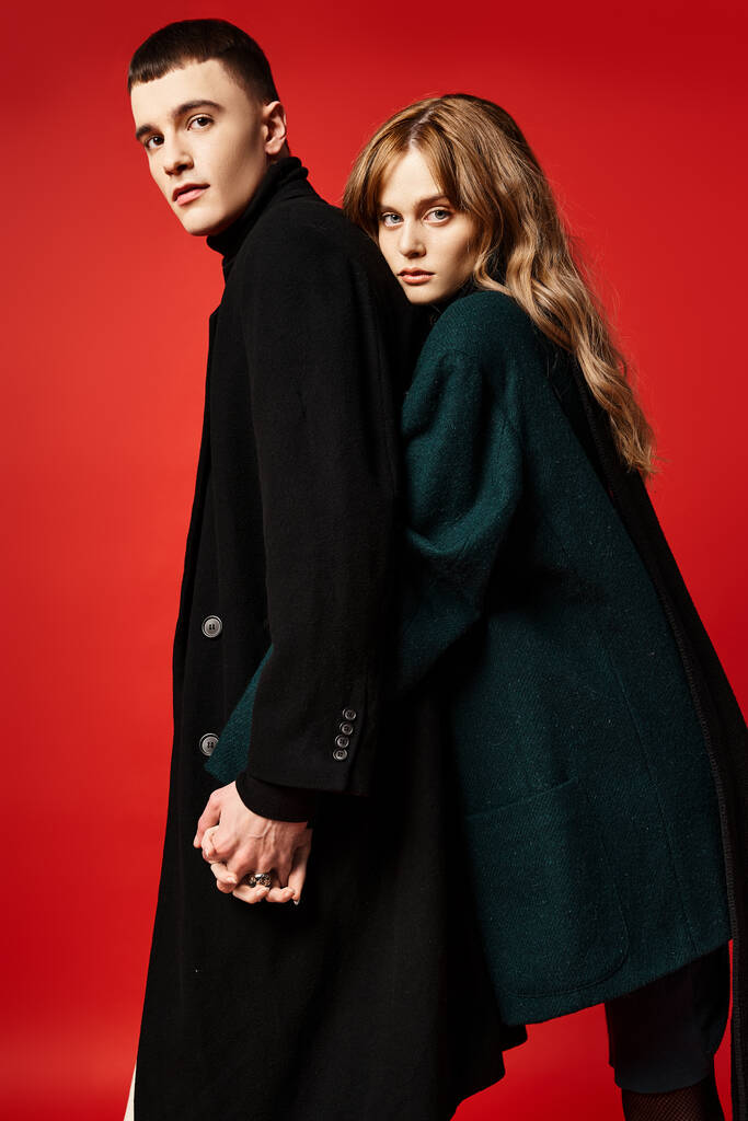csábító szerető pár kifinomult elegáns kabátok nézi kamera piros élénk háttér - Fotó, kép