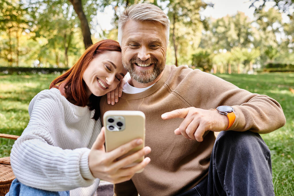 Una pareja en atuendo casual se toma románticamente una selfie con un teléfono celular en el parque. - Foto, imagen