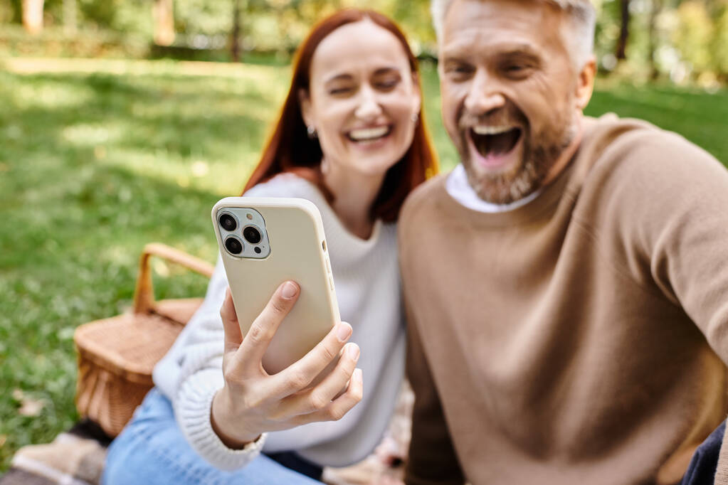 Un hombre captura un momento alegre mientras se toma una selfie con una mujer en un exuberante entorno de parque. - Foto, imagen