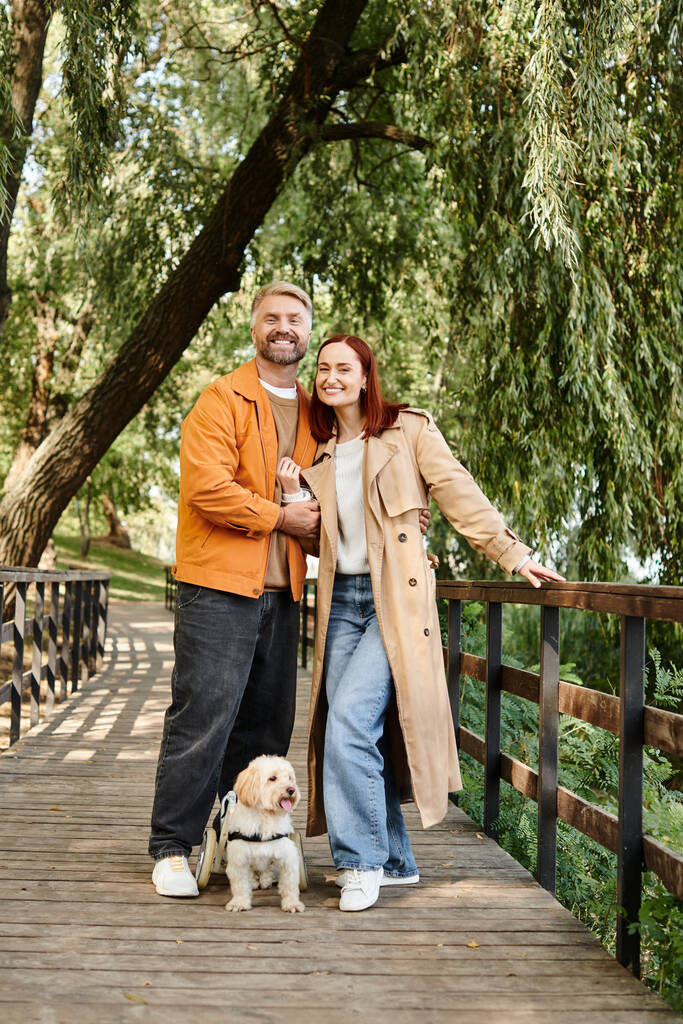 Erwachsenes Paar in Freizeitkleidung steht mit seinem geliebten Hund auf einer Brücke. - Foto, Bild