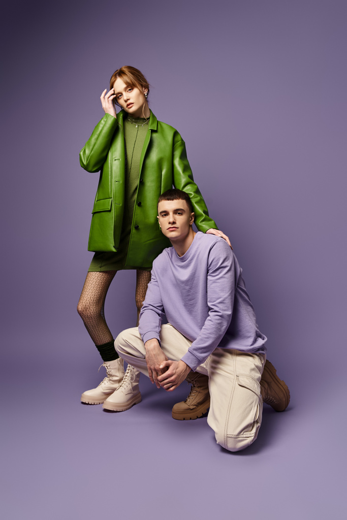 fashionable couple in vibrant clothes posing together on purple background and looking at camera - Photo, Image