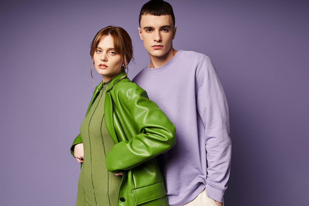 couple à la mode dans des vêtements vibrants posant ensemble sur fond violet et regardant la caméra - Photo, image
