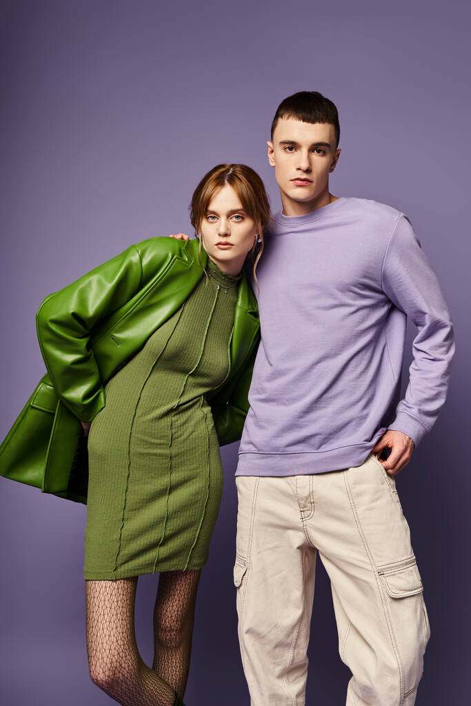 well dressed couple in vibrant clothes posing together on purple background and looking at camera - Photo, Image