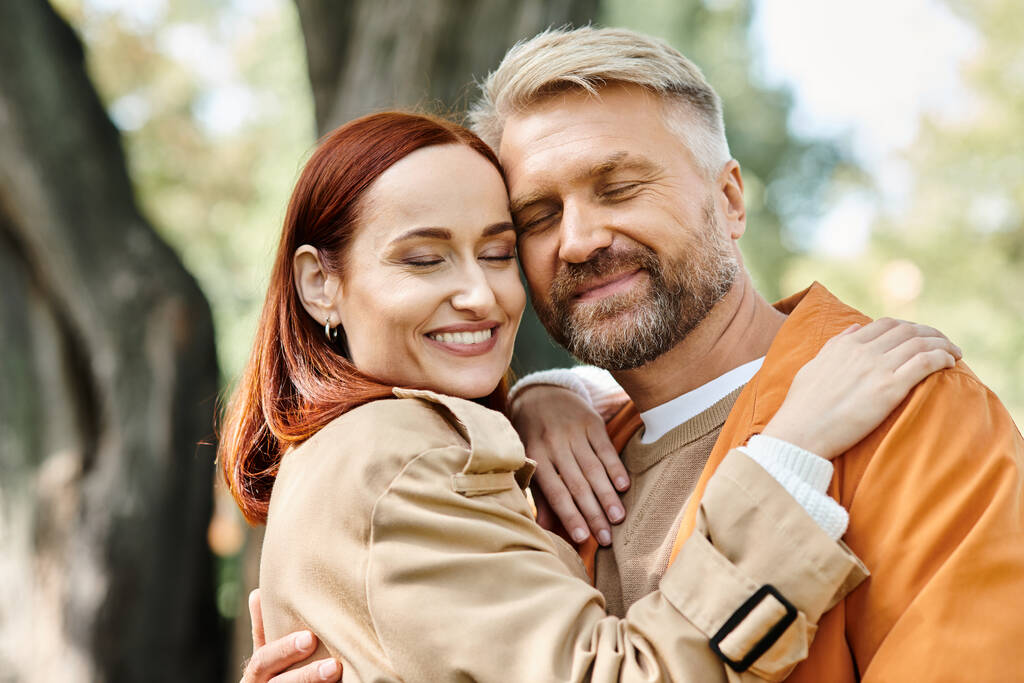 Ein Mann und eine Frau in legerer Kleidung umarmen sich beim Spaziergang in einem Park liebevoll. - Foto, Bild