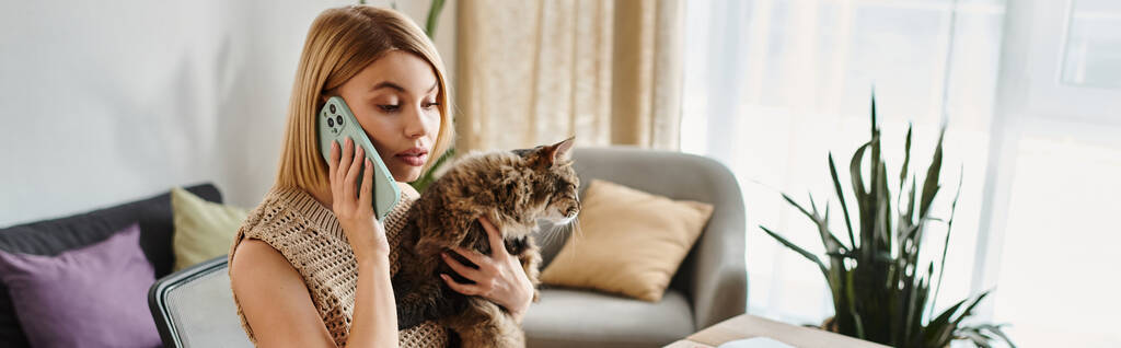 Eine stylische Frau mit kurzen Haaren, die mit ihrem Handy chattet, während sie zu Hause ihre entzückende Katze knuddelt. - Foto, Bild