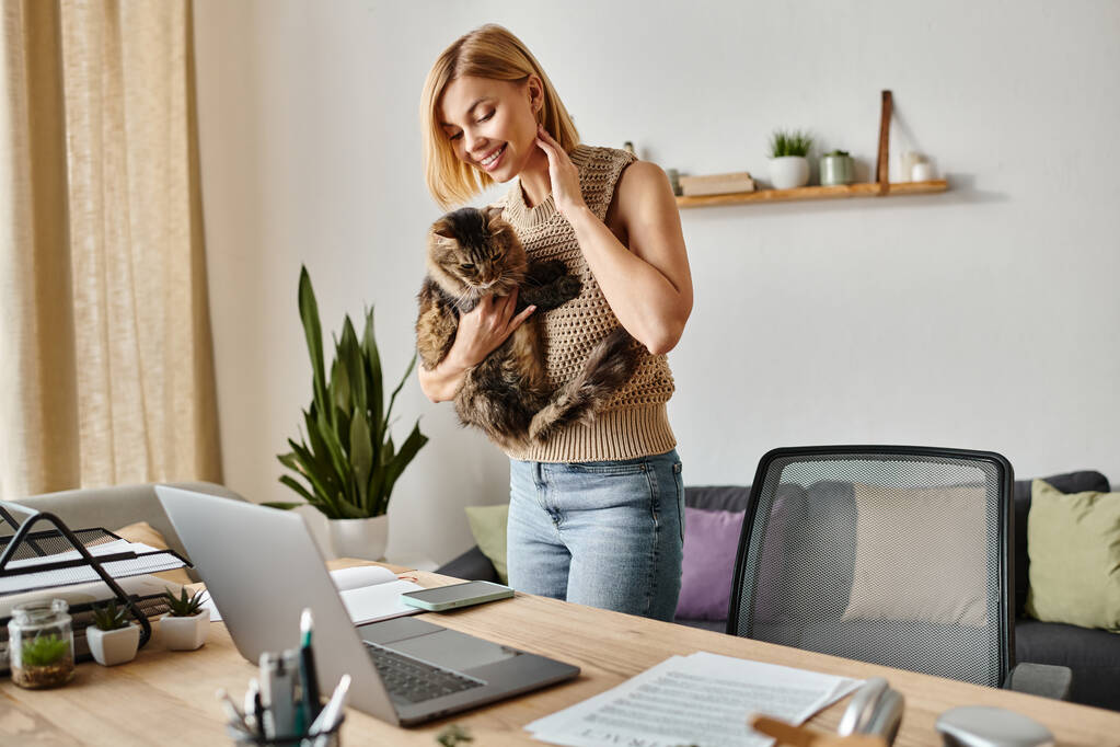 Een vrouw houdt haar kat liefdevol vast terwijl ze thuis bij een laptop staat. - Foto, afbeelding