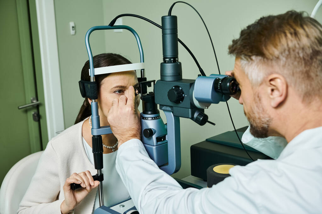 Мужчина изучает женщину через свои инструменты в кабинете врача для лазерной коррекции зрения. - Фото, изображение