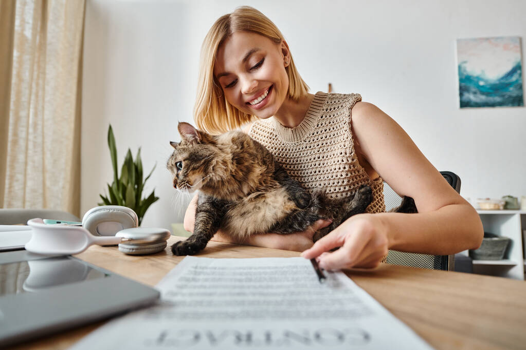 Tyylikäs nainen lyhyet hiukset rauhallisesti istuu pöydässä, mukana hänen kissan kumppani. - Valokuva, kuva