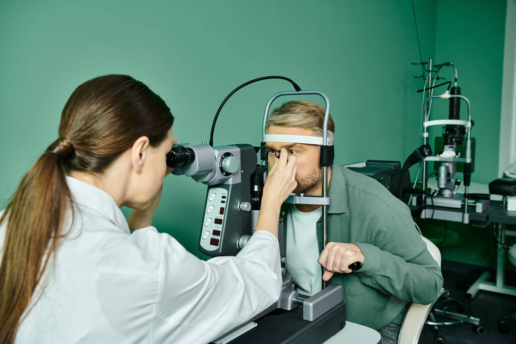 Kobieta bada oczy mężczyzn przez mikroskop w gabinecie lekarskim w celu laserowej korekcji wzroku. - Zdjęcie, obraz
