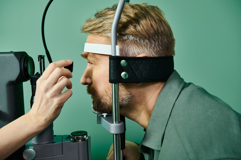 Αφιερωμένο γιατρός εξετάζει τα μάτια mans μέσα από ένα μικροσκόπιο σε ένα γραφείο γιατρών για διόρθωση όρασης λέιζερ. - Φωτογραφία, εικόνα
